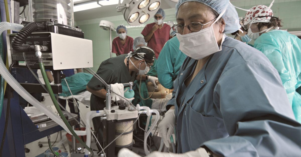 Anestesiologista ao lado do aparelho de anestesia em sala de procedimento com equipe médica