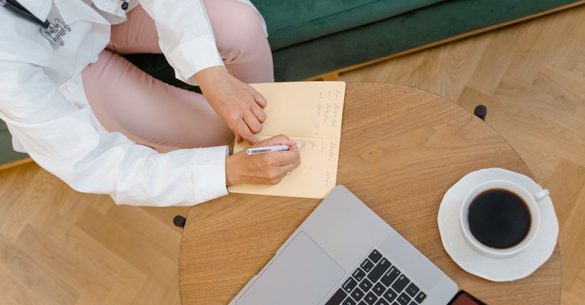 Médico em consultório conferindo planilha financeira em notebook com calculadora sobre a mesa