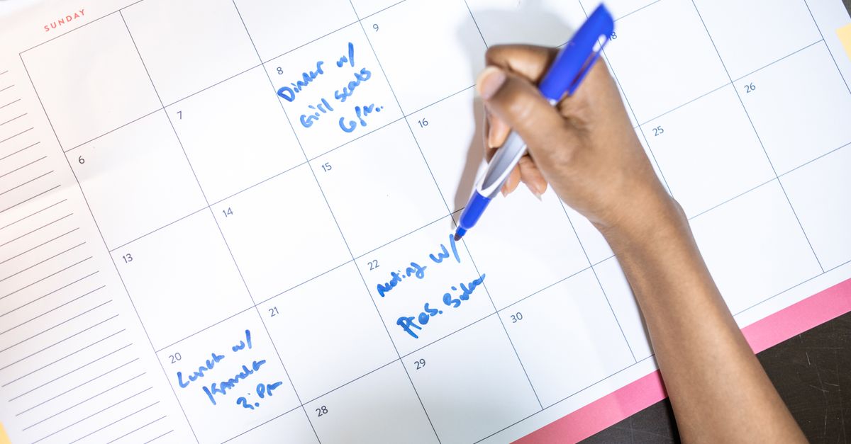Mão anotando compromissos em calendário mensal com caneta azul