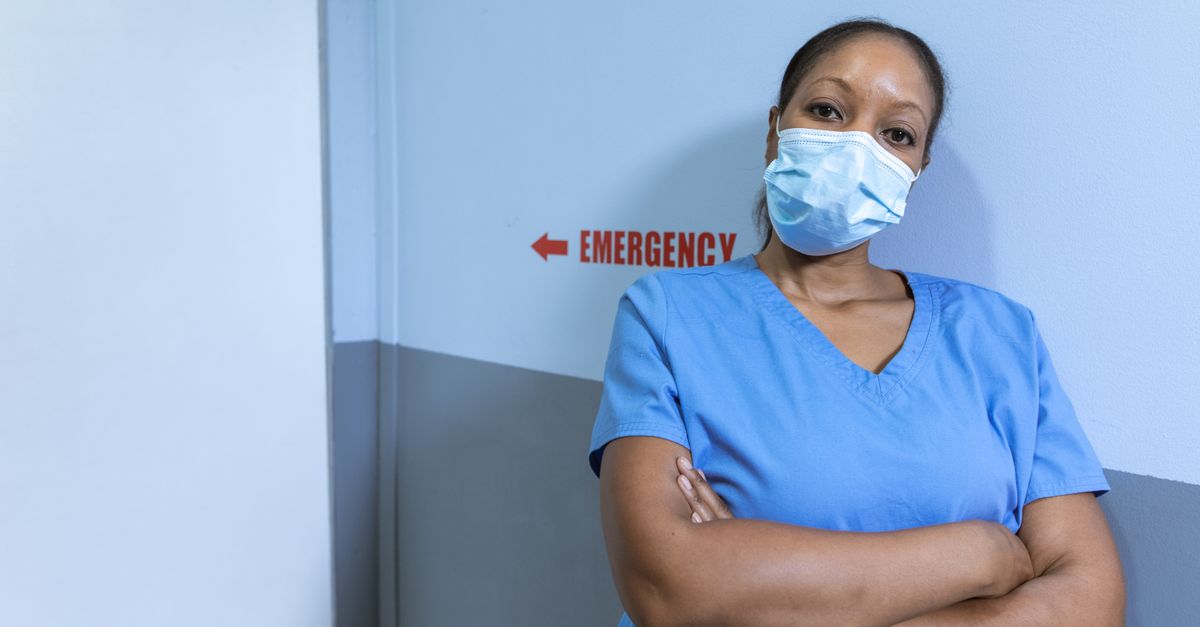 Profissional de saúde de máscara e uniforme azul em corredor de emergência de hospital